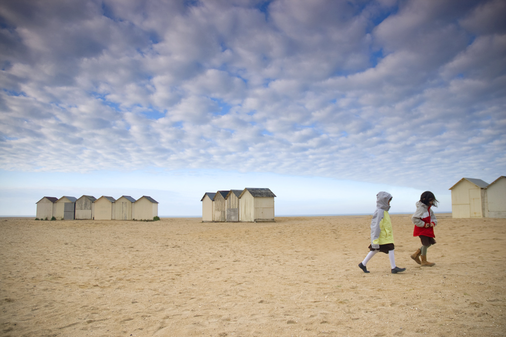2 girls walking a windswept beach, Ouistreham, Normandy, France
